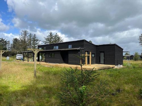 een klein zwart huis in een veld met een auto bij JB365-Fjerritslev-Hedestien-9 in Torup Strand
