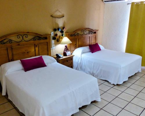 a bedroom with two beds with white sheets and purple pillows at Hotel Hacienda Bugambilias in La Paz