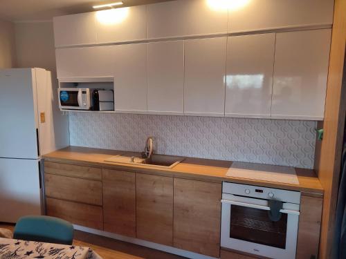 a kitchen with white cabinets and a sink and a refrigerator at Apartament Jasny Spokój in Jantar