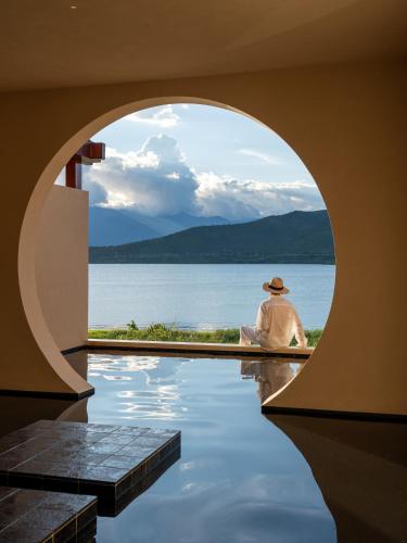 a man sitting on the floor of a building looking at the water at 大理空山语 风眠艺术海景酒店 Dali Kongshanyu Art Seaview Hotel in Dali Airport