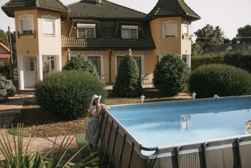 a woman standing next to a swimming pool in front of a house at Villa Maranga in Dombóvár