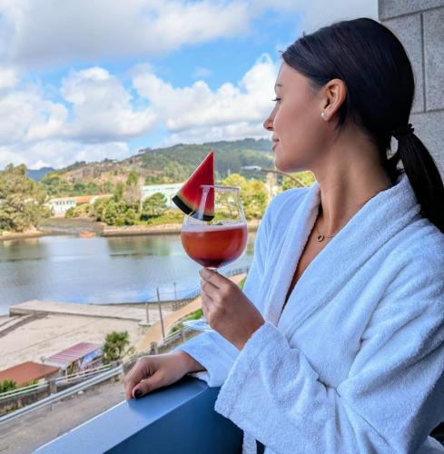 a woman in a bathrobe holding a glass of wine at Hotel SPA GBC Arcade in Arcade