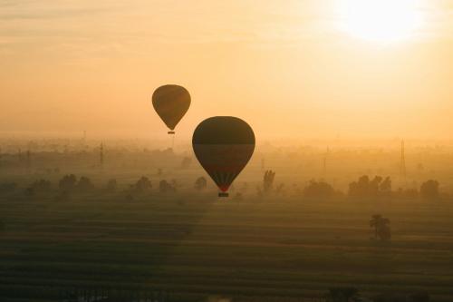 two hot air balloons flying over a field at sunset at White Gorf Hotel in Luxor
