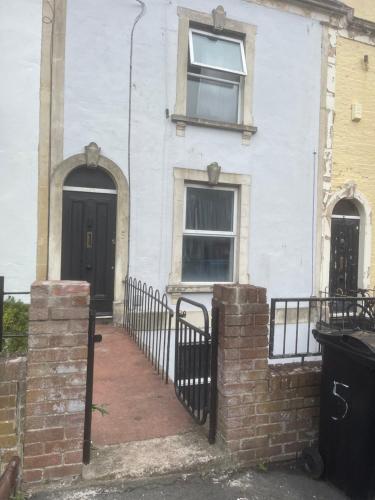 a white house with two black doors and a fence at 5 Brunswick St - Bedroom 02 downstairs in Bristol