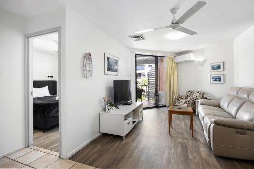 a white living room with a couch and a tv at The Beach Retreat Coolum in Coolum Beach
