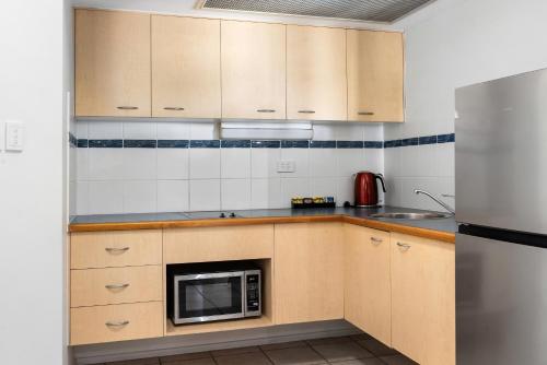 a kitchen with wooden cabinets and a microwave at The Beach Retreat Coolum in Coolum Beach
