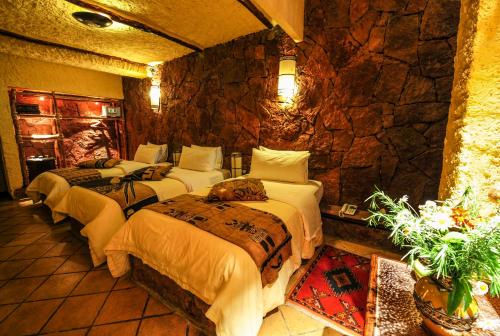 a bedroom with three beds and a stone wall at Hotel Xaluca Dades in Boumalne
