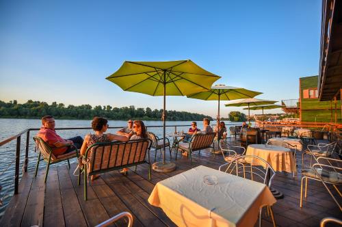 a group of people sitting on a dock with tables and umbrellas at San Art Floating Hostel & Apartments in Belgrade