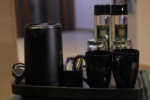 a tray with two black coffee mugs and glasses at Hotel Bilton Wilson Garden Near Nimhans Hospital in Bengaluru