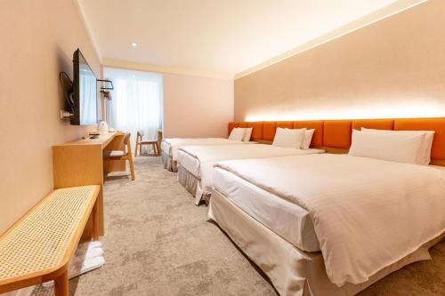 a hotel room with three beds and a desk at Hotel Tainan in Tainan
