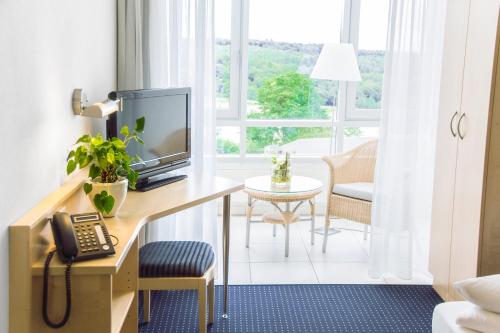 a room with a desk with a tv and a phone at Stausee-Hotel in Metzingen