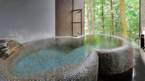 a large stone bath tub in a room with a window at Onsen Glamping ShimaBlue in Nakanojo