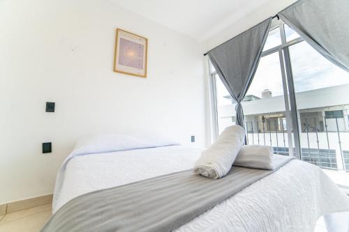 a white bedroom with a bed and a large window at Hotel Catedral Jojutla in Jojutla
