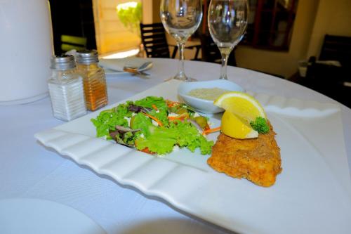a white plate with fish and salad on a table with wine glasses at Masai Shuttles And Hotel in Polokwane