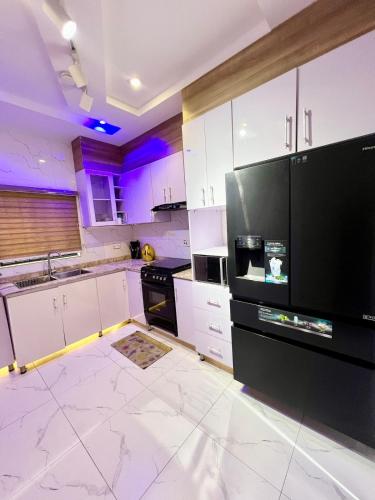 a kitchen with white cabinets and a black refrigerator at Luxury Smart 3-Bedroom Semi-Detached Apartment in Abuja