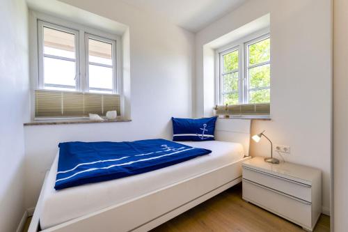 a white bedroom with a bed and two windows at Haus Wind&Wellen, Wohnung Hafen in Wittdün