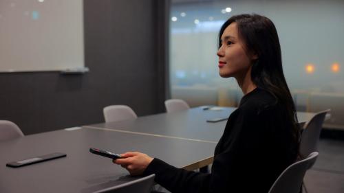 a woman sitting at a table holding a remote control at Workers Hotel Daejeon by Aank in Daejeon