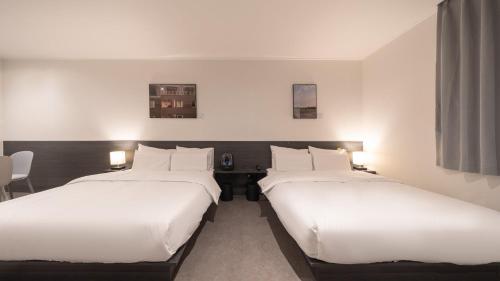 two beds in a hotel room with white sheets at Workers Hotel Daejeon by Aank in Daejeon