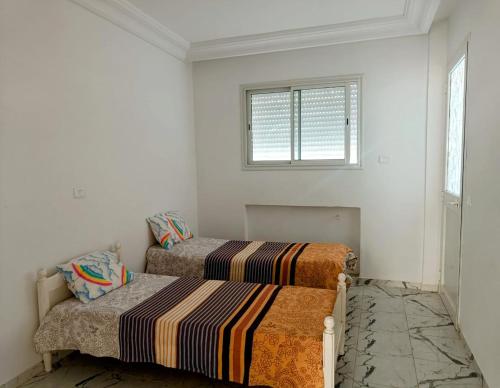 two beds in a white room with a window at Appartement a Hammamet Lux in Hammamet