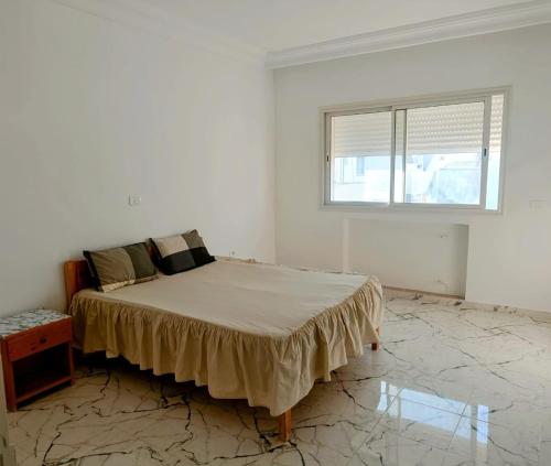 a white bedroom with a bed and a window at Appartement a Hammamet Lux in Hammamet