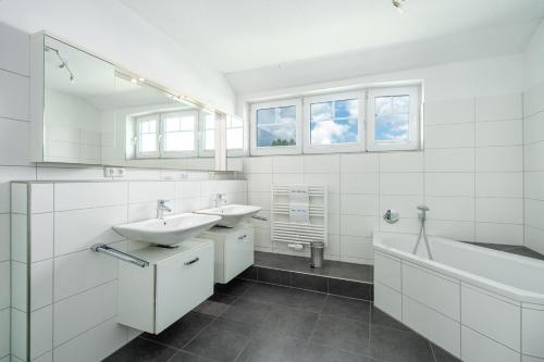 ein weißes Badezimmer mit zwei Waschbecken und einer Badewanne und einer Badewanne in der Unterkunft Ferienhaus "Stella Olivia" in Lobbe