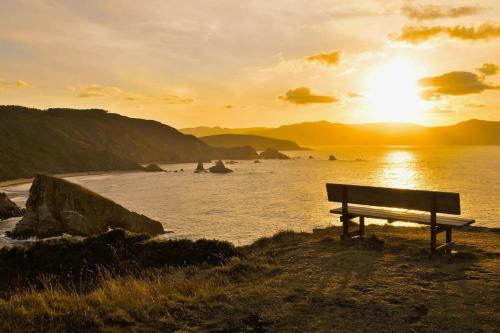 a bench sitting on the beach with the sunset at The Cliffs - Cala Porto do Val in O Vicedo