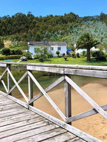 a bridge over a river with a house in the background at The Cliffs - Esteiro Saltwater Beach in O Barqueiro