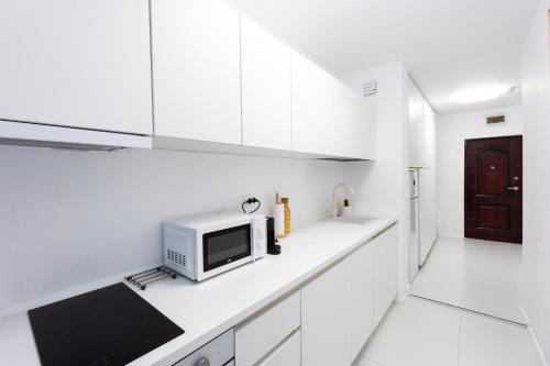 a white kitchen with white cabinets and a microwave at Lun Apartment in Cluj-Napoca