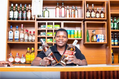 a man behind a bar holding two bottles of alcohol at Via Alpina Lodge Makuti Ltd in Kisumu