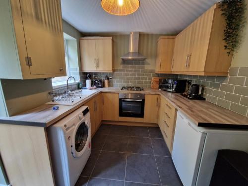 a kitchen with wooden cabinets and a washer and dryer at Chic 2 Bedroom Close to Town with Free Parking in Tredegar