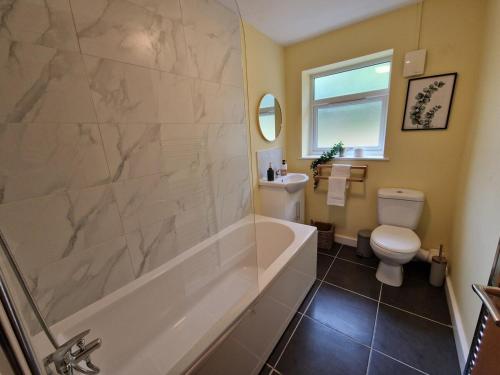 a bathroom with a tub and a toilet and a sink at Chic 2 Bedroom Close to Town with Free Parking in Tredegar