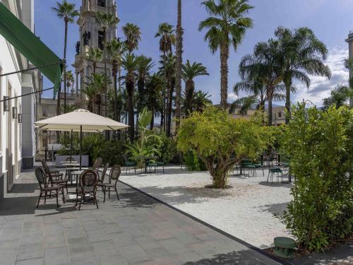 a patio with a table and chairs and palm trees at Habita79 Hotel Pompeii - MGallery Collection in Pompei