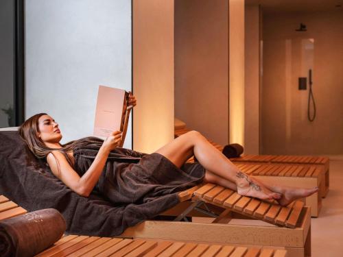 a woman laying on a bed reading a book at Habita79 Hotel Pompeii - MGallery Collection in Pompei