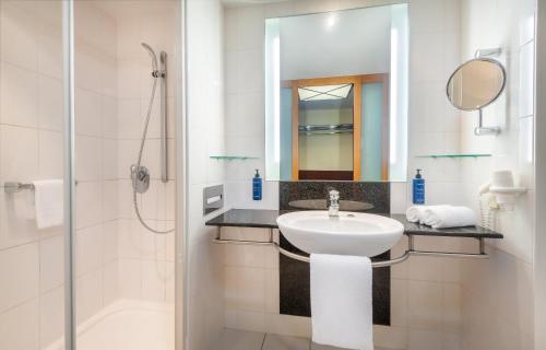 a white bathroom with a sink and a shower at Radisson Blu Fürst Leopold Hotel in Dessau