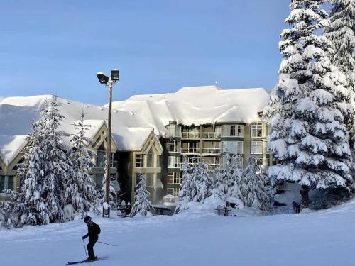 a man riding skis in the snow in front of a building at Woodrun Lodge 216 | Renovated Ski-In Ski-Out Condo w/ Free Parking, Pool, Hot Tub, & Gym in Whistler