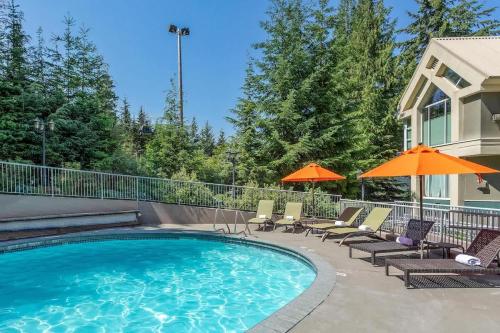 a swimming pool with chairs and umbrellas next to a house at Woodrun Lodge 216 | Renovated Ski-In Ski-Out Condo w/ Free Parking, Pool, Hot Tub, & Gym in Whistler