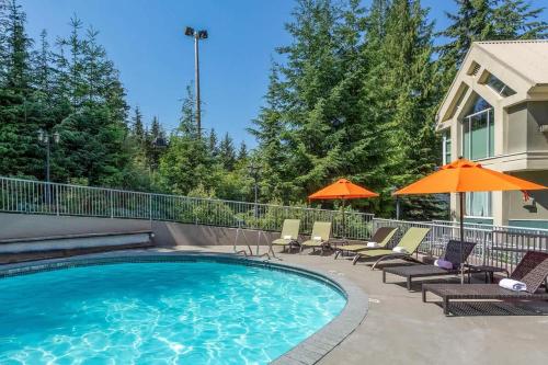a swimming pool with chairs and umbrellas next to a house at Woodrun Lodge 211 | Ski-In Ski-Out Condo w/ Heated Pool, Hot Tub, Parking, & Gym in Whistler