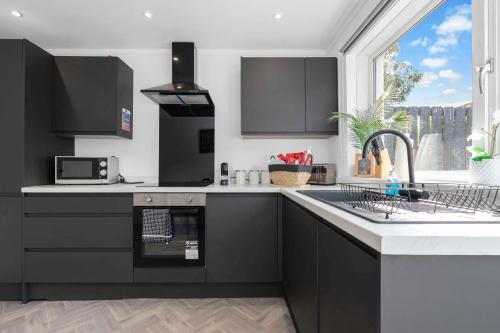 a kitchen with black cabinets and a sink and a window at Vacant Nests The Livingston Retreat Wi-Fi in Uphall