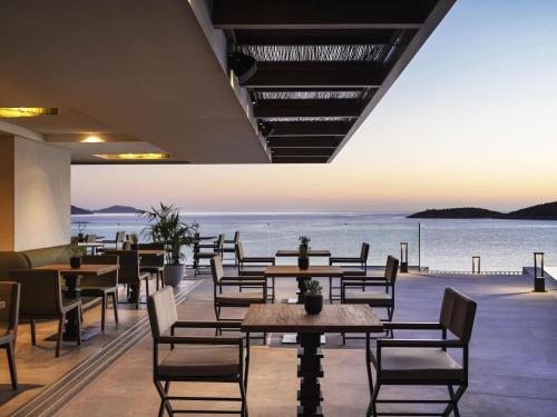 a restaurant with tables and chairs and a view of the water at NIKO Seaside Resort MGallery in Agios Nikolaos