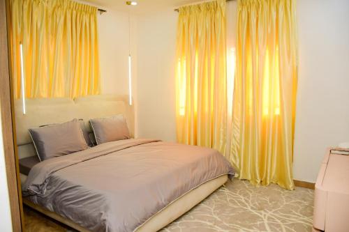a bedroom with a large bed with yellow curtains at Winters Apartment in Abuja