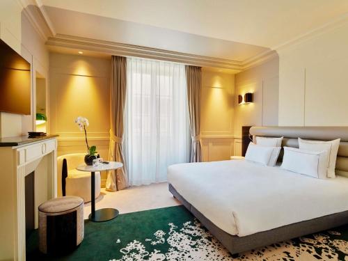 a hotel room with a large white bed and a fireplace at La Licorne Hotel & Spa Troyes - MGallery Collection in Troyes