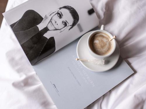 a cup of coffee sitting on top of a magazine at Le Louise Hotel Brussels - MGallery Collection in Brussels