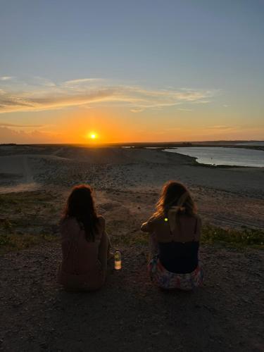 two women sitting on the beach watching the sunset at Bangalôs Flecheiras de Canaã in Flecheiras