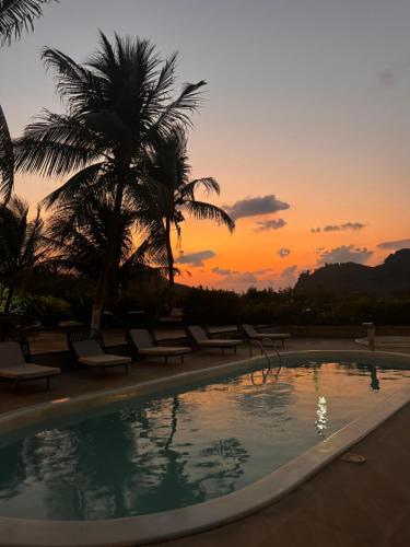 a pool with chairs and palm trees at sunset at Pousada Liberty Noronha in Fernando de Noronha