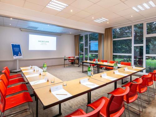 a conference room with tables and chairs and a projection screen at Mercure Strasbourg Aéroport in Ostwald