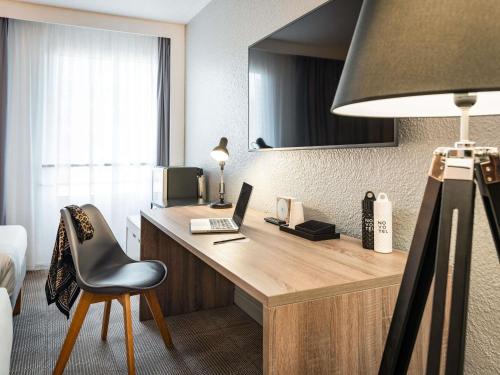 a hotel room with a desk with a laptop and a chair at Novotel Paris Est in Bagnolet