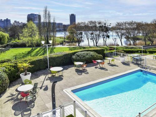 a swimming pool with tables and chairs on a patio at Novotel Paris Créteil Le Lac in Créteil