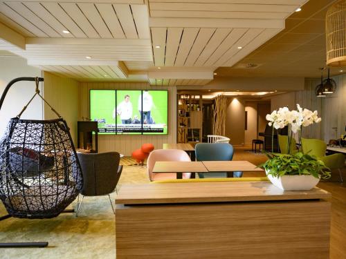 a lobby with a tv and chairs and tables at Novotel Paris Créteil Le Lac in Créteil