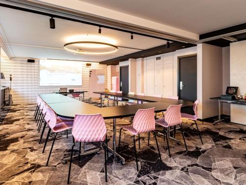 a conference room with a table and pink chairs at Novotel Marne La Vallée Collégien in Collégien