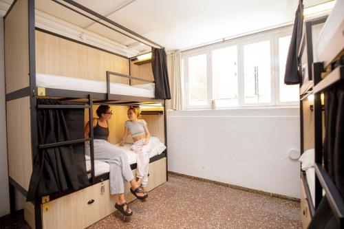 two women sitting on bunk beds in a bus at Onefam Les Corts in Barcelona